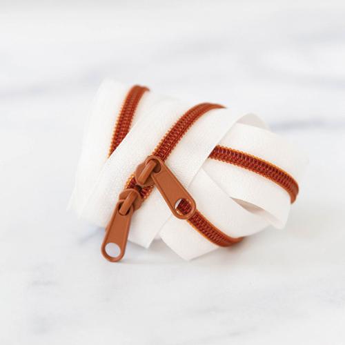 White zipper tape with two amber colored zipper pulls on a white background.