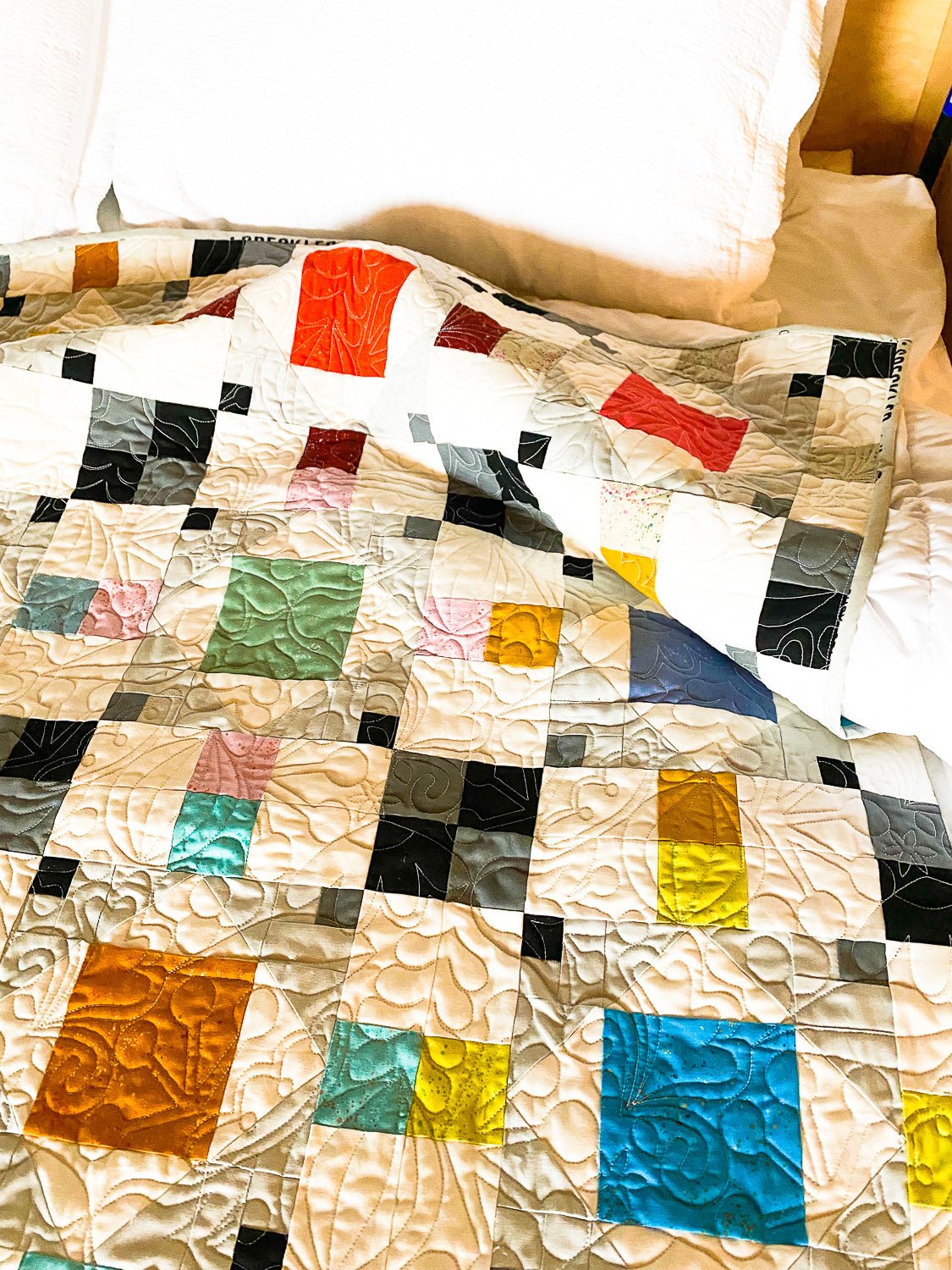 Modern patchwork quilt displayed on a bed, using the Koselig quilt pattern with soft neutral fabrics and longarm quilting.