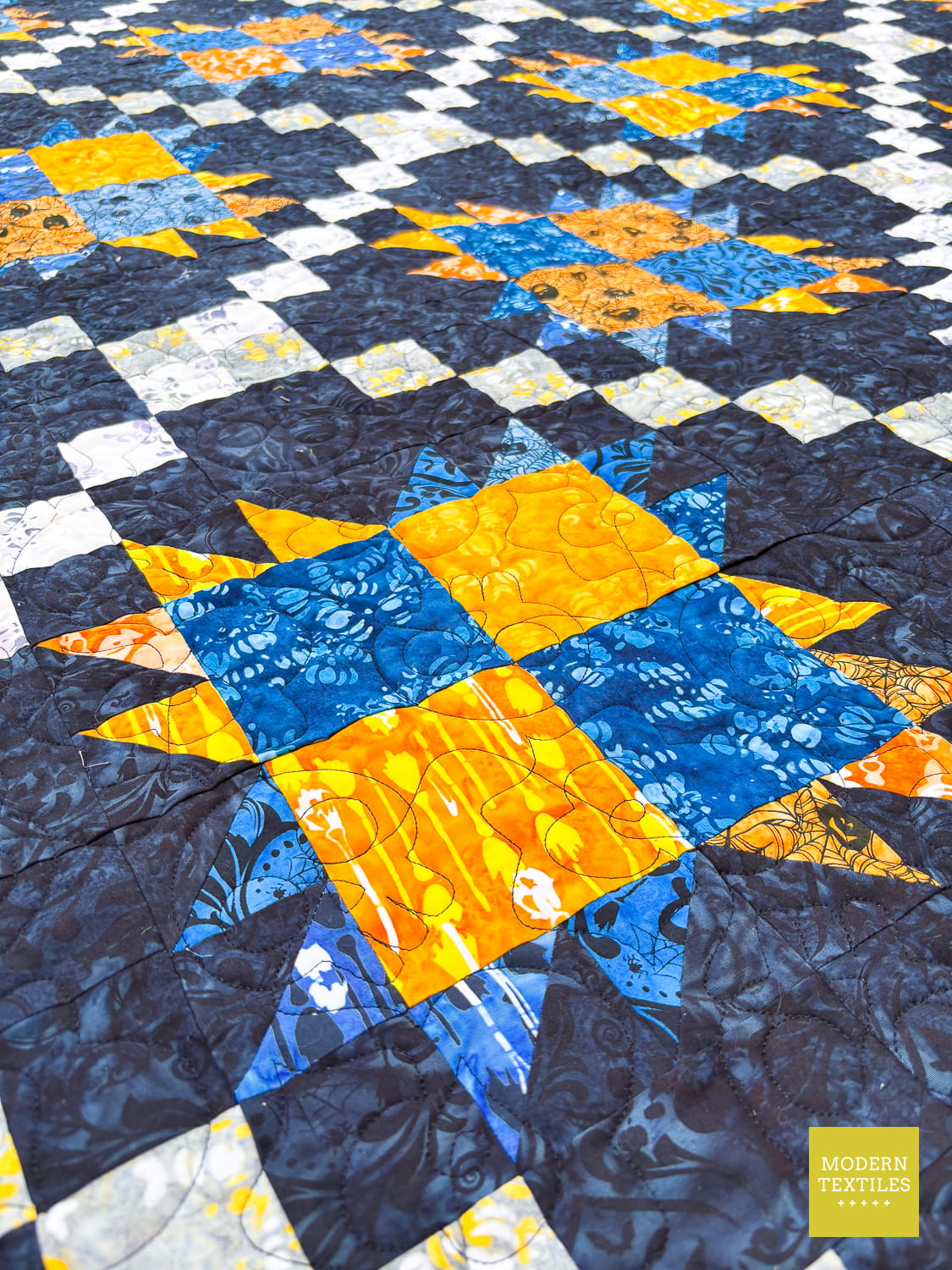 Bear Paw Irish Chain quilt with blue, orange, and white pattern on a black background, highlighting the skulls and roses quilting.