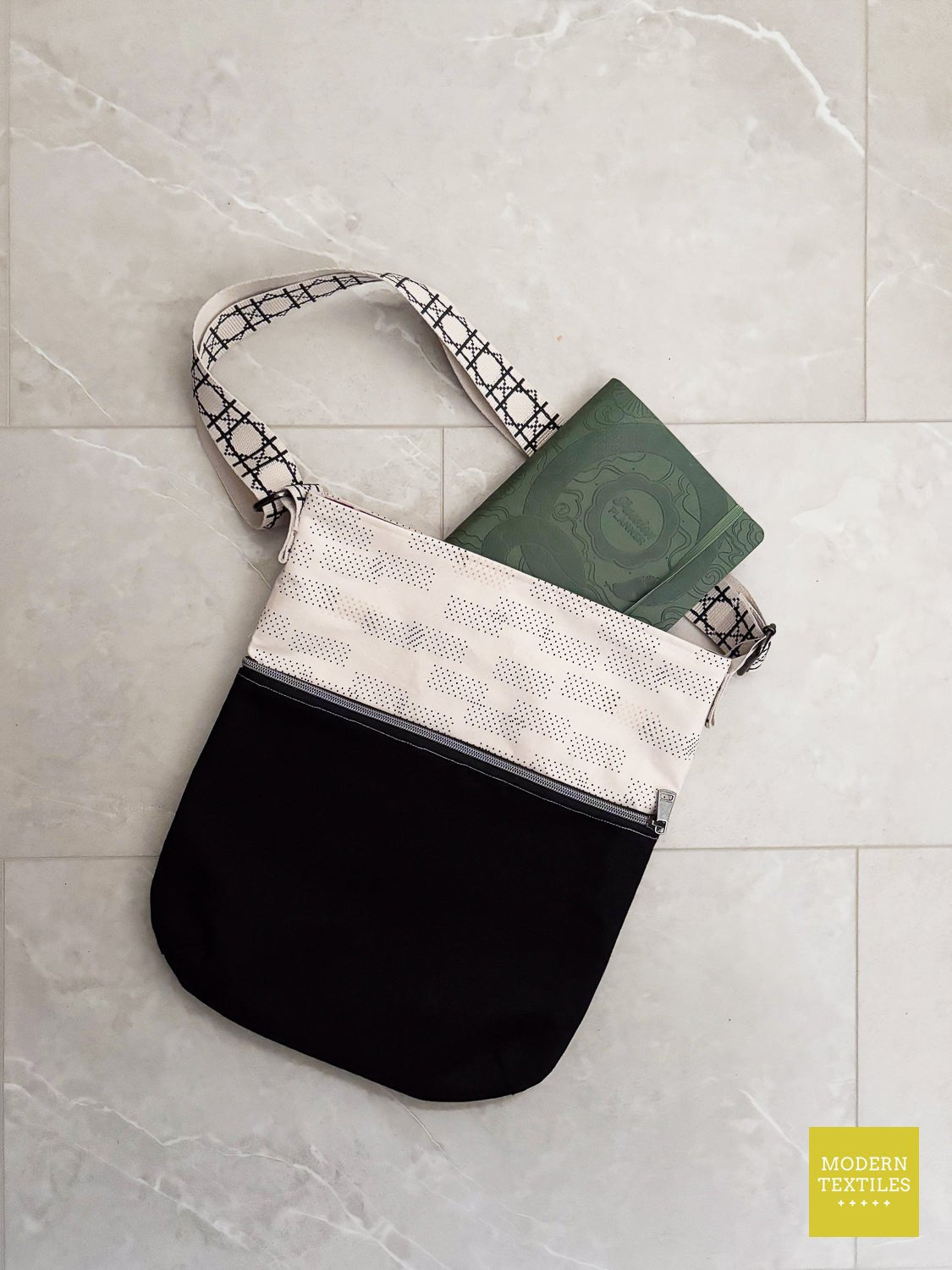 Connection Bag crossbody purse with black lower panel and light top fabric, holding a book to show capacity.