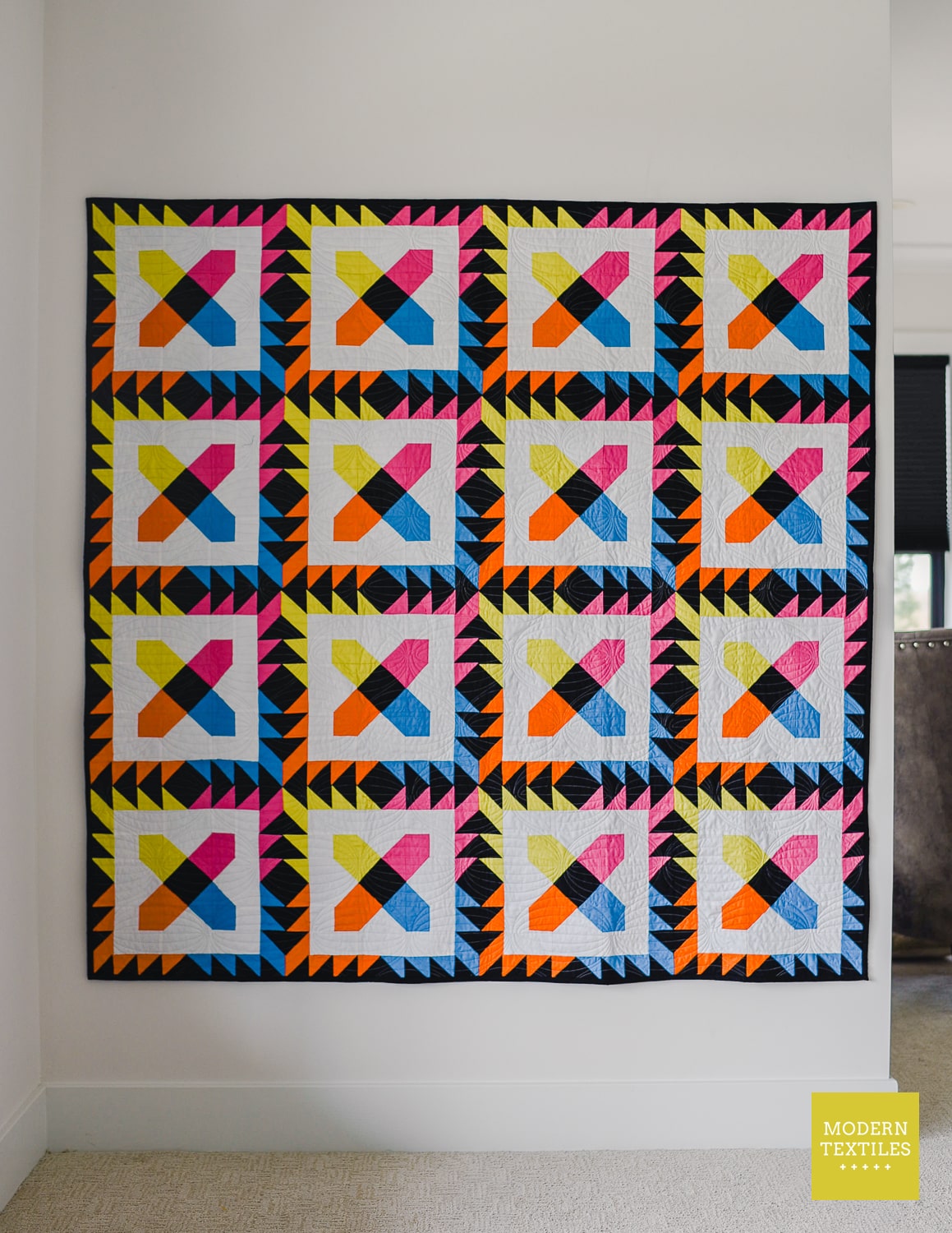 Full image of bold and bright patchwork quilt hanging on white wall.