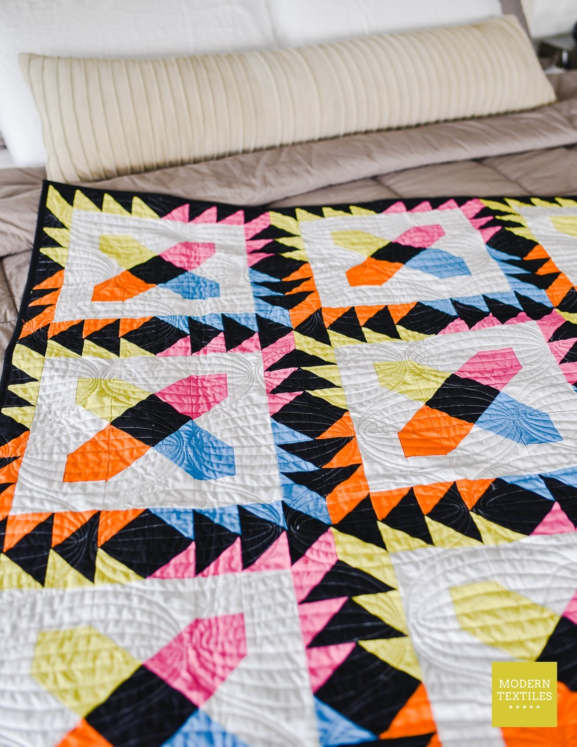 Bright patchwork modern quilt laid on top of bed showcasing the bright fabrics and texture from longarm quilting.
