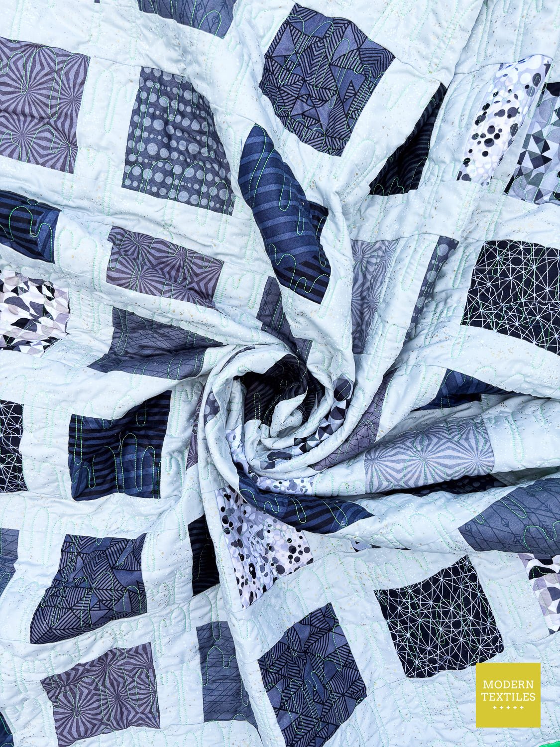 Close-up of modern charm pack quilt showing geometric blocks and longarm quilting texture.