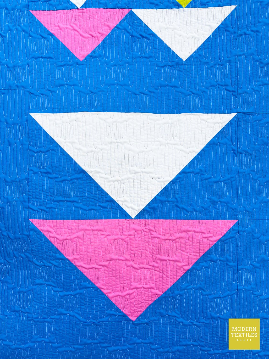 Close-up of large triangle blocks in white and pink on a textured blue Exploratory quilt background.