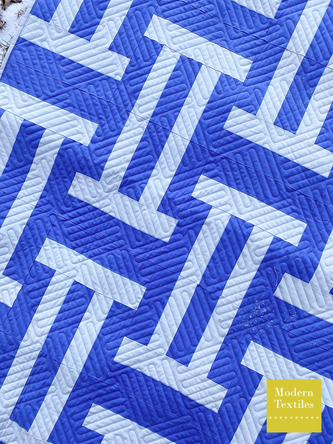 Close-up of Cake Weave quilt showing blue woven blocks and textured longarm quilting.