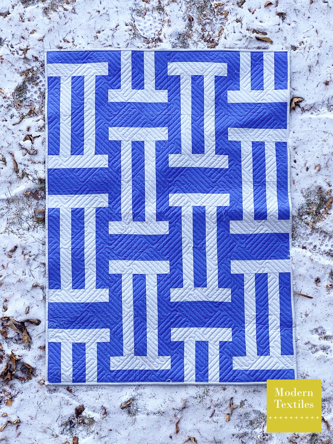 Close-up of Cake Weave quilt showing blue woven blocks and textured longarm quilting.