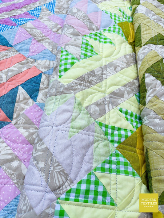 Close-up of a modern pastel and green patchwork quilt professionally quilted by Modern Textiles, showing detailed geometric stitching and scrappy prints.