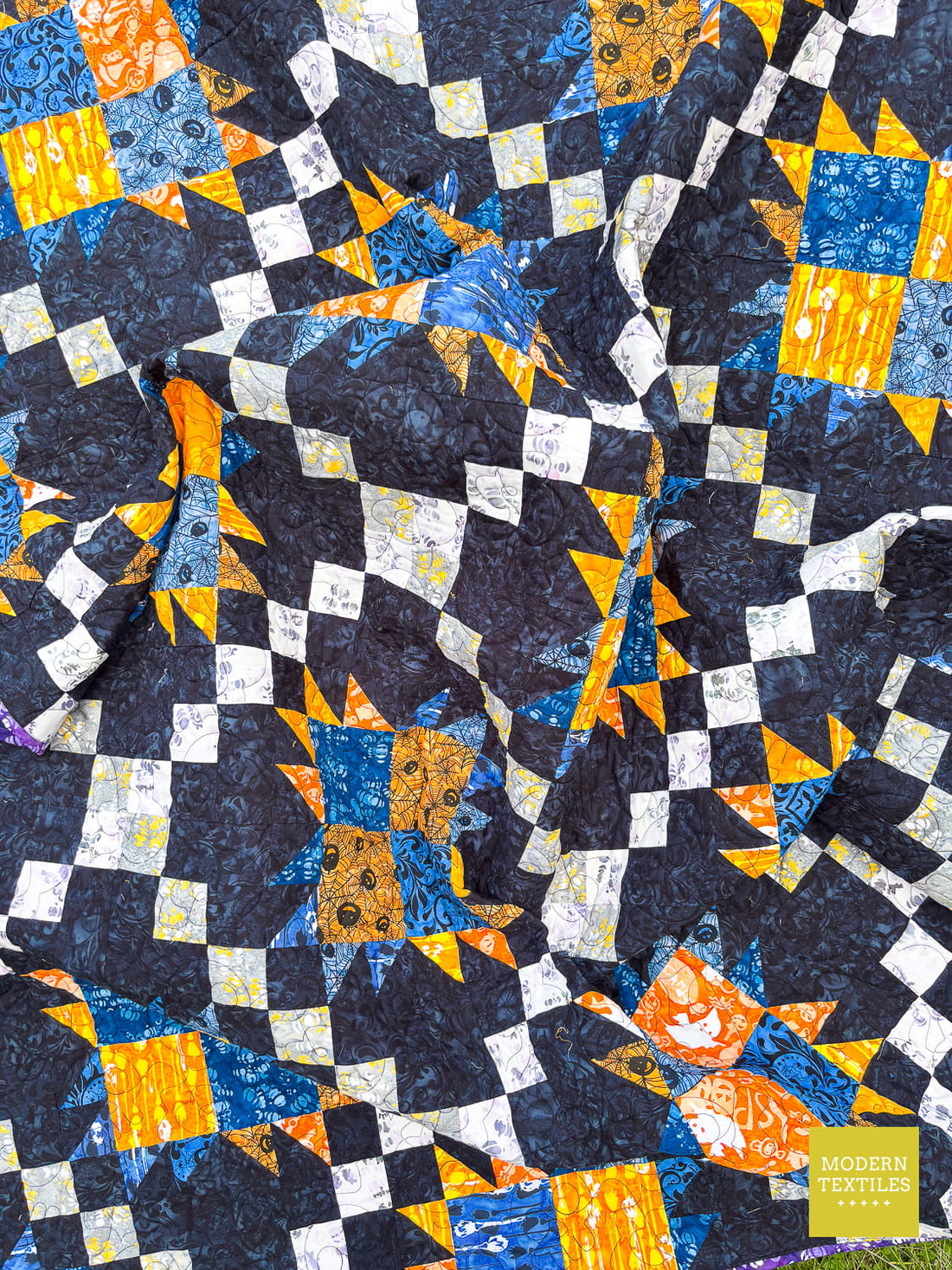 Black background quilt with orange, blue, white and grey accent fabrics creating a patchwork bear paw and irish chain modern quilt.
