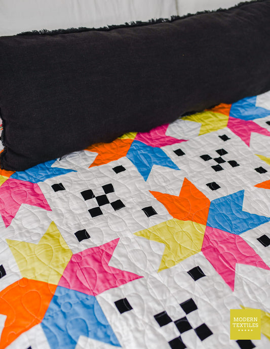 Detail image of patchwork portion of the quilt and the colorful stars on the Four Corner Stars, black pillow in background on top of quilt.