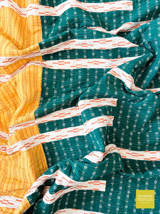 Crinkled flat lay of a modern linen quilt with bold stripe piecing, daisy print fabric, and dense longarm quilting.
