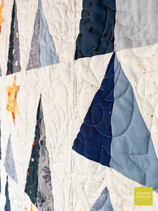 Close up of a winter-themed tree quilt with blue and white patchwork trees and longarm quilting.