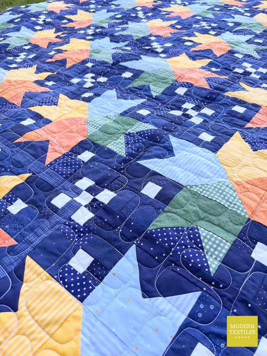 Modern star quilt pattern shown at a diagonal with scrappy layout in navy, baby blue, orange, yellow, and pine green, showcasing organic stacked stone quilting design.