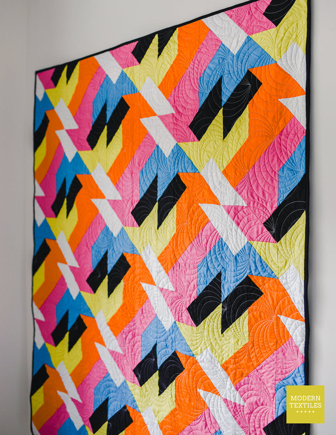 Close-up angled view of the Sheared modern quilt pattern showing bold geometric patchwork in bright pink, orange, yellow, blue, and black fabrics.