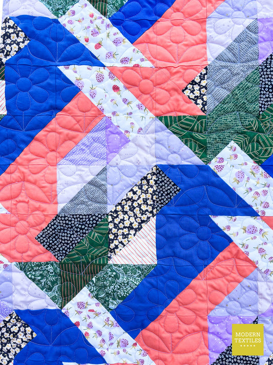 Close-up of scrappy quilt  using pops of bright blue and coral and detailed stitches of daisy quilting pantograph.