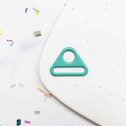 Turquoise metal triangle ring on a white surface with colorful confetti