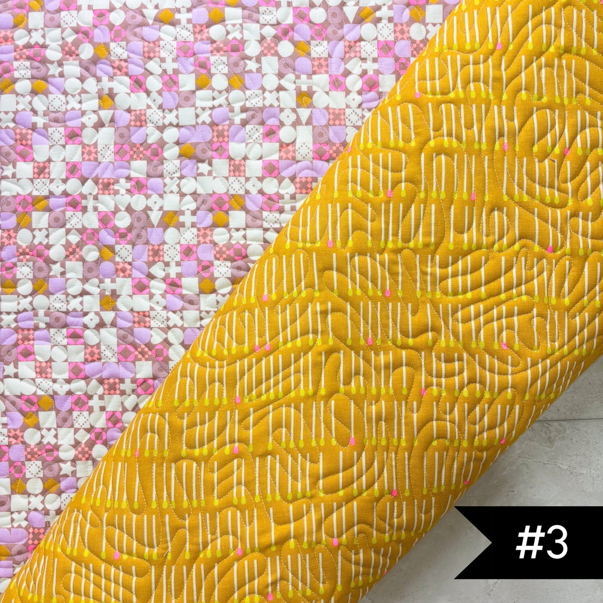 A quilted fabric panel shown diagonally, featuring a bright yellow lining fabric with white stitched meander quilt patnto and a pink, white, and yellow patchwork printed exterior. #3 in white on a black tag on lower right hand corner.