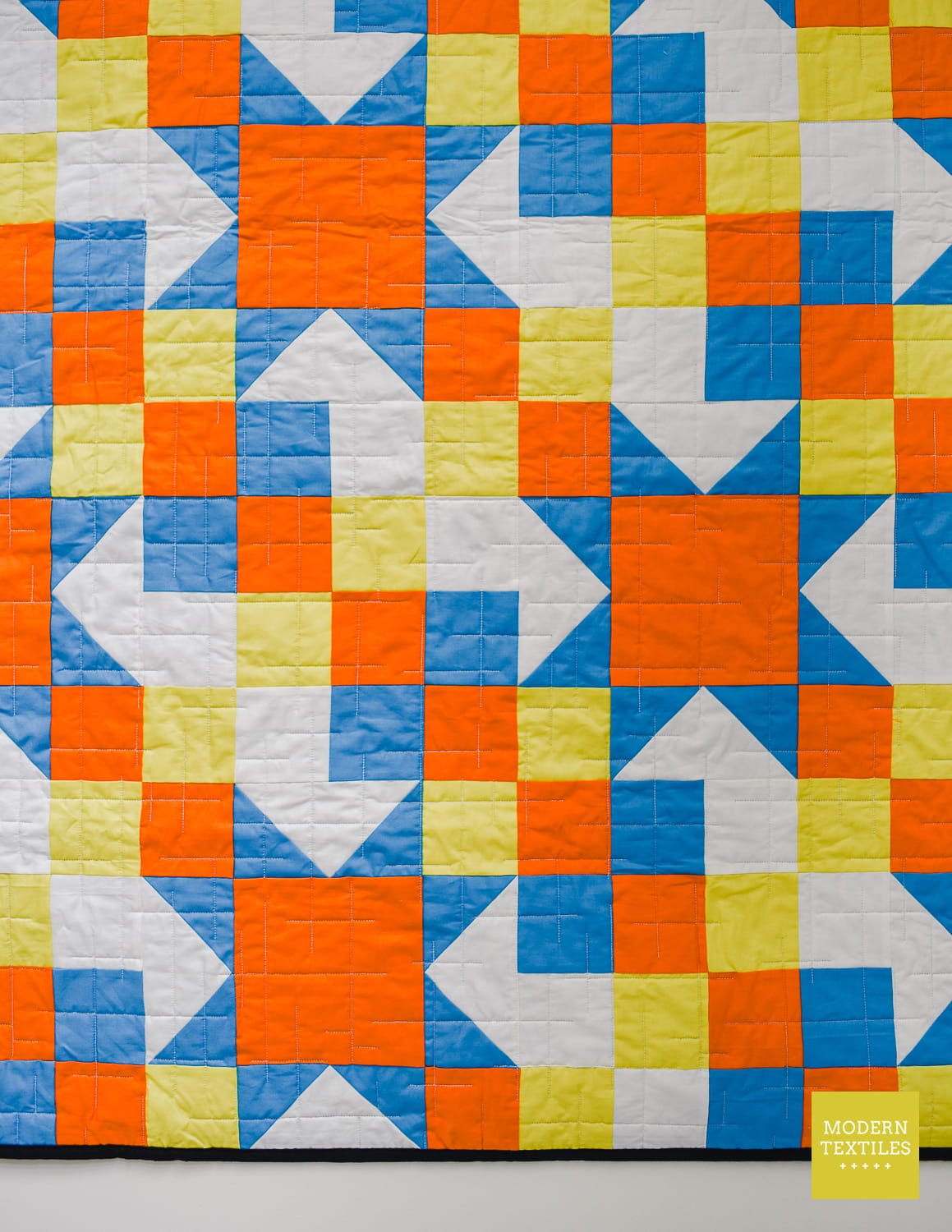 A close-up of a quilted fabric featuring a colorful geometric pattern of orange, blue, yellow, and white blocks.