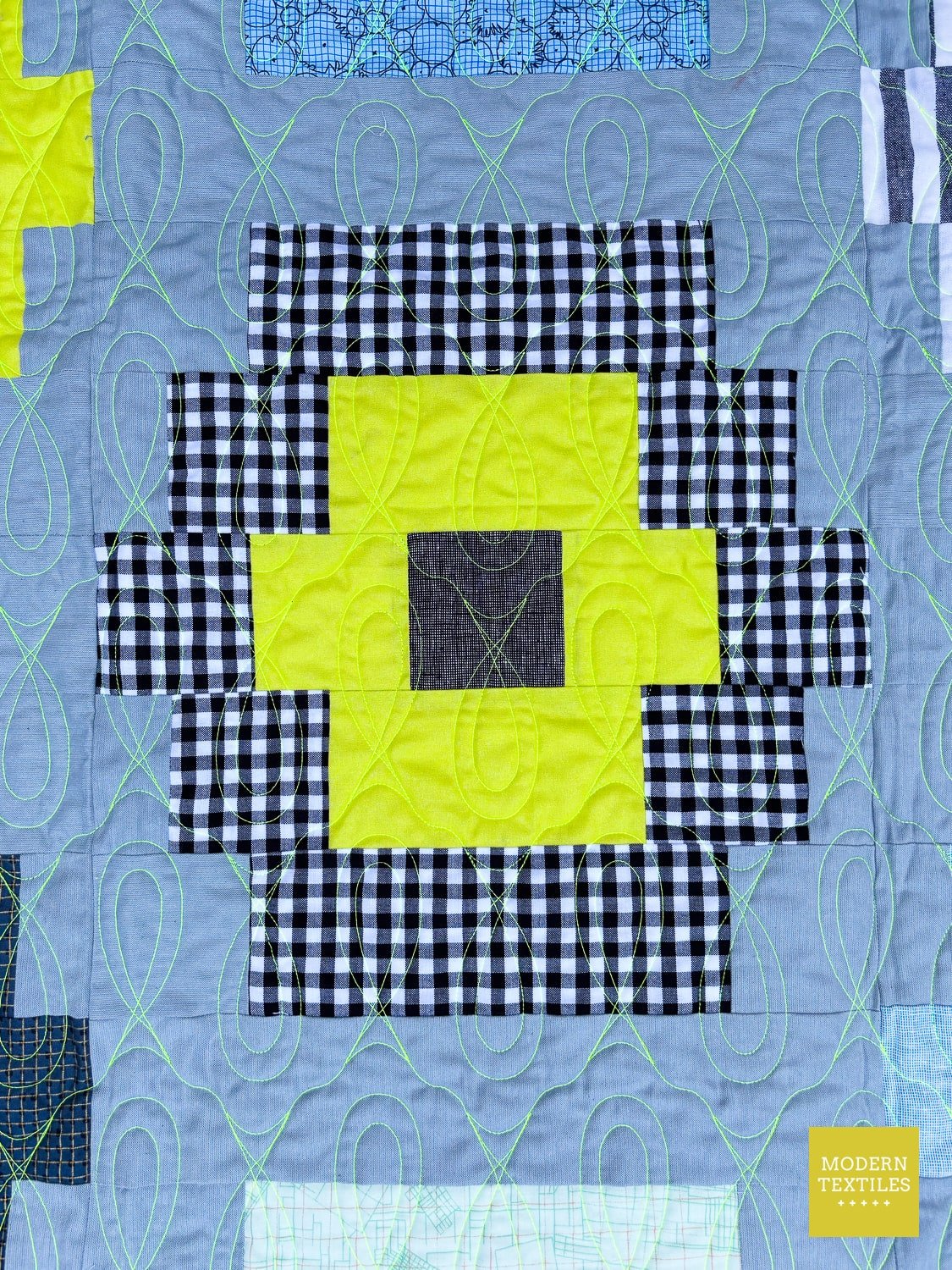Quilt with geometric pattern featuring black, white, and yellow blocks on a blue-grey background.