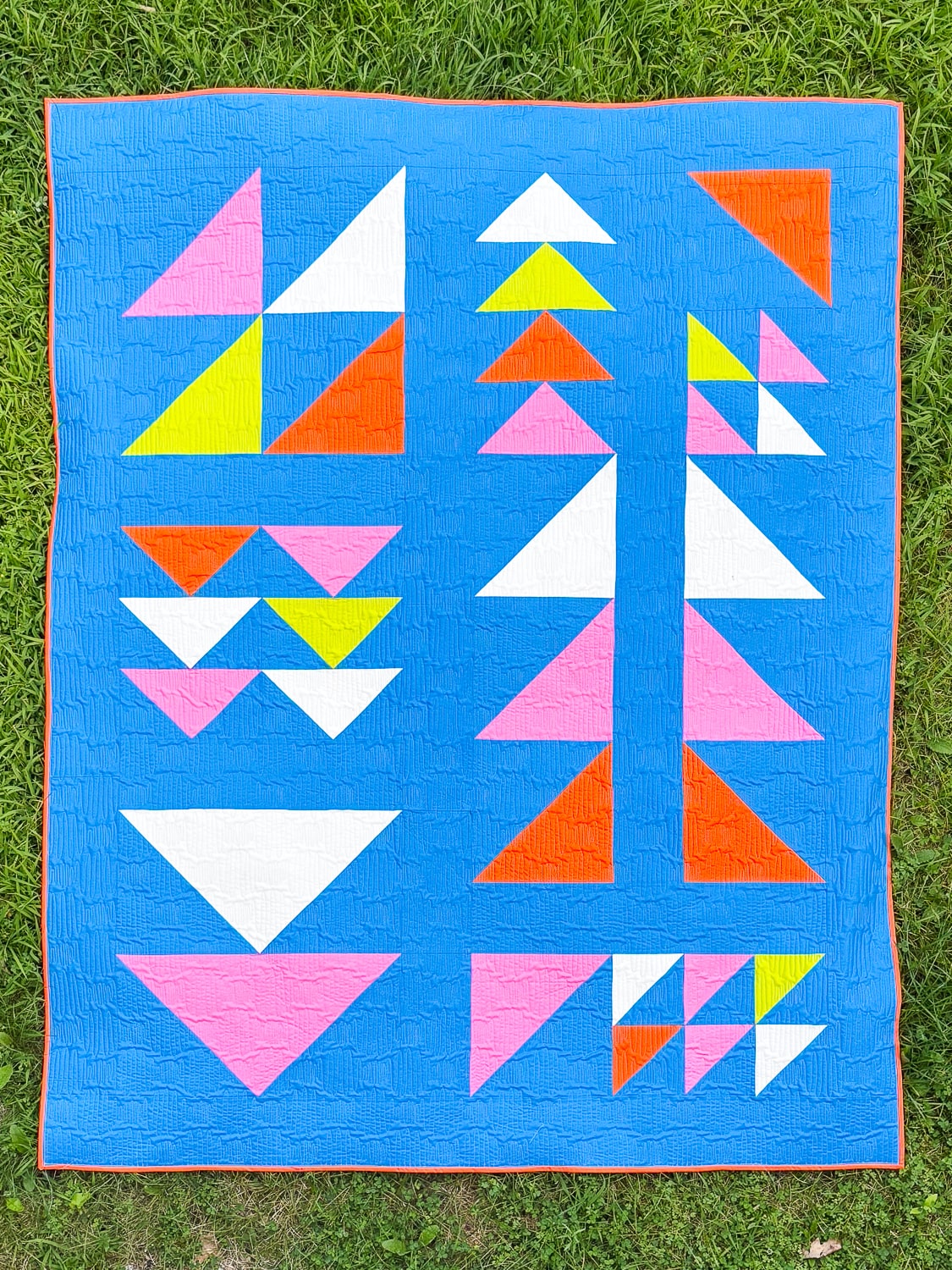 A bright modern quilt featuring rows of colorful geometric triangles on a vivid blue background, quilted with a textured longarm design.
