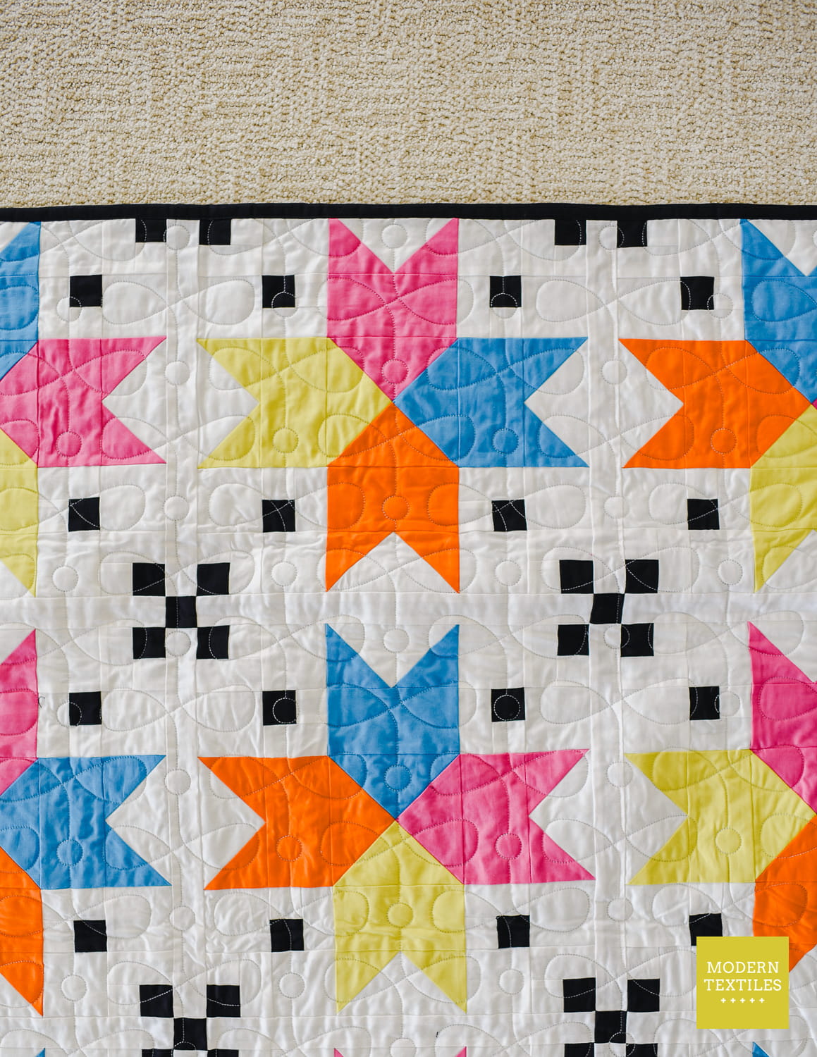 Colorful Four Corner Stars quilt with geometric pattern on a natural color berber rug.