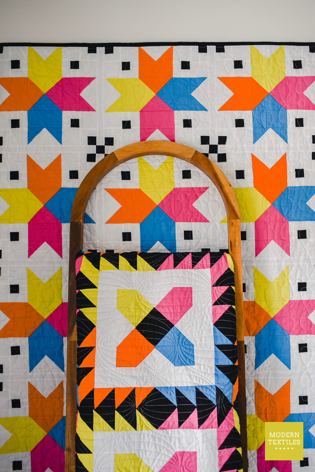 Four Corner Stars Quilt haning on wall, with wood quilt ladder holding folded Checkered Paws quilt both in bright fabrics.