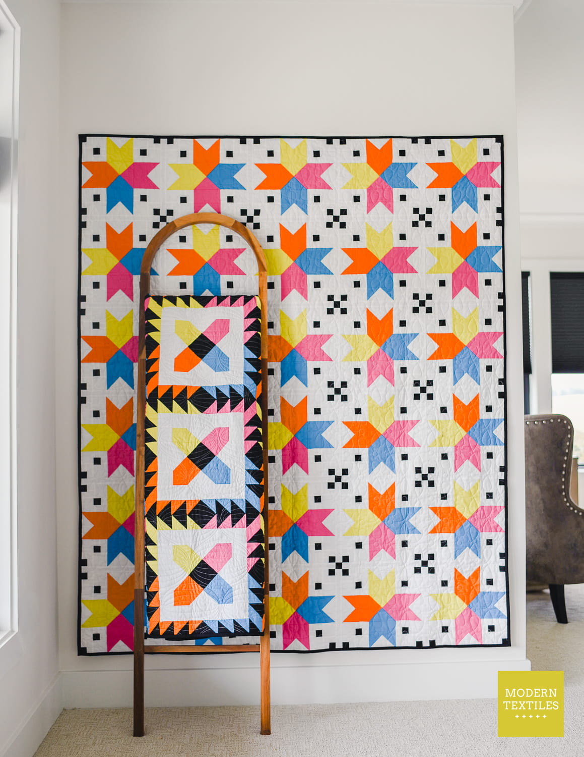 Four Corner Stars quilt hanging on white wall with quilt ladder leaning against the quilt with Checkered Paws quilt folded and hanging on quilt ladder.