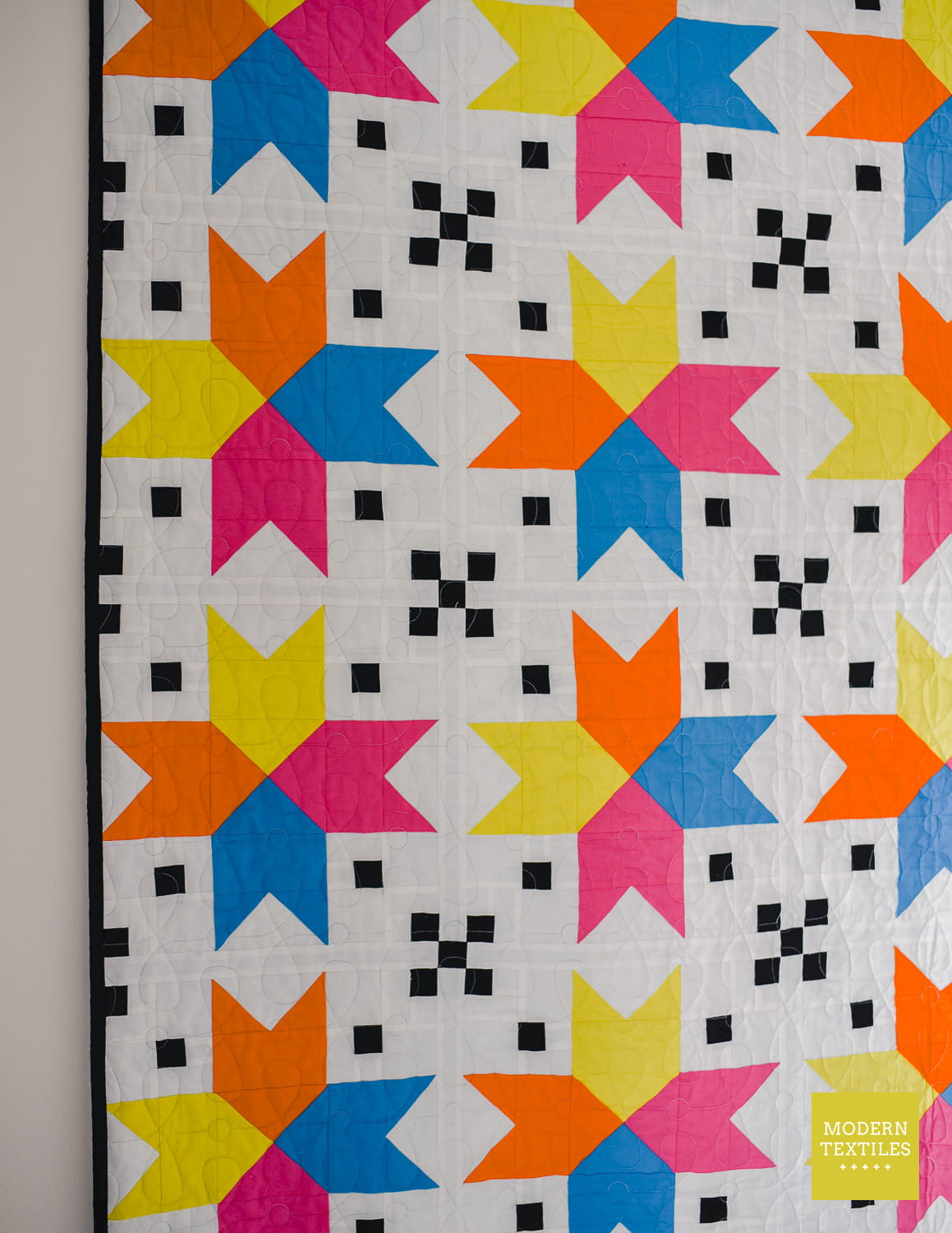 Four Corner Stars quilt with blue, hot pink, bright yellow/green and orange against white background fabric and black accent checkered blocks.
