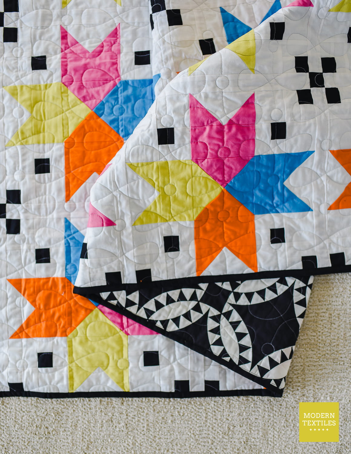 Colorful star quilt folded over showing the back of the quilt which is black and white geometric print.