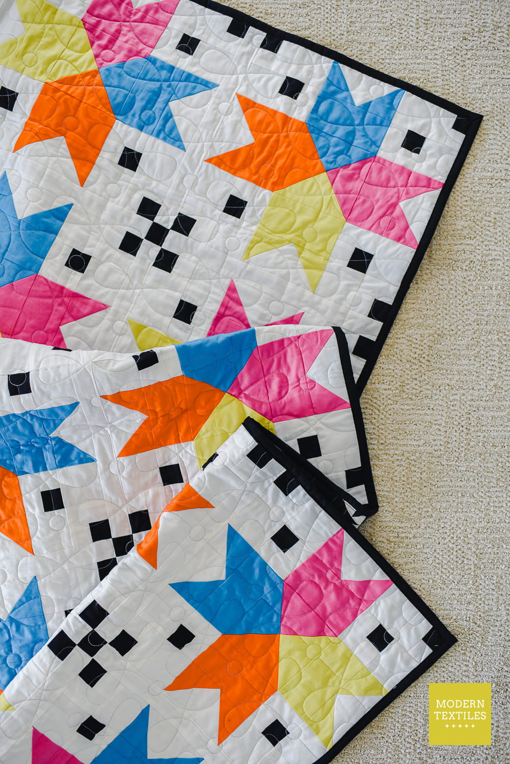 Colorful quilt with star patterns folded onto itself a few times showing texture and dimension of quilt and quilting.