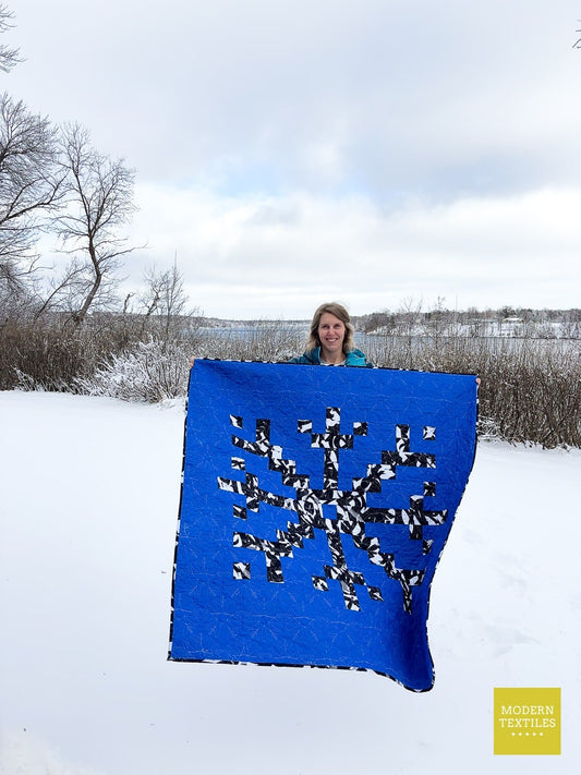 Person holding a blue quilt with a snowflake design in a snowy landscape