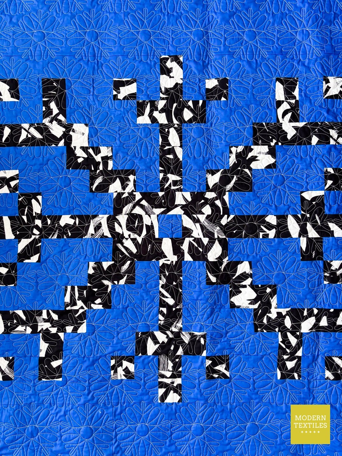 Quilt with black, white, and blue snowflake motif on a blue background.