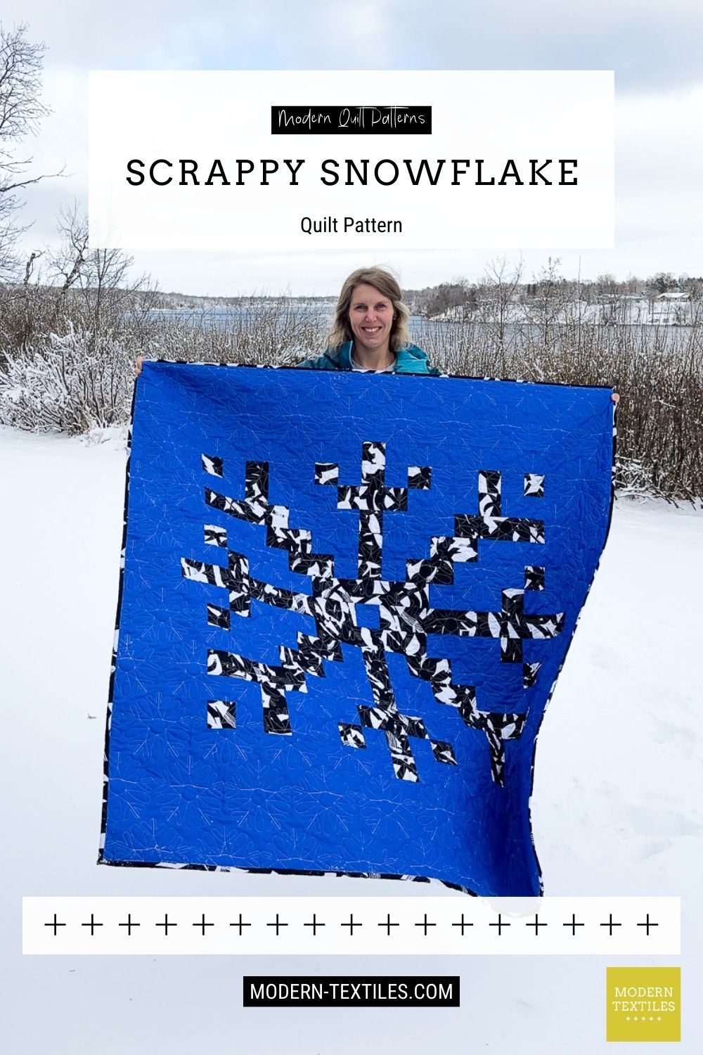 Person holding a blue quilt with a snowflake pattern in a snowy landscape, featuring Modern Textiles branding.
