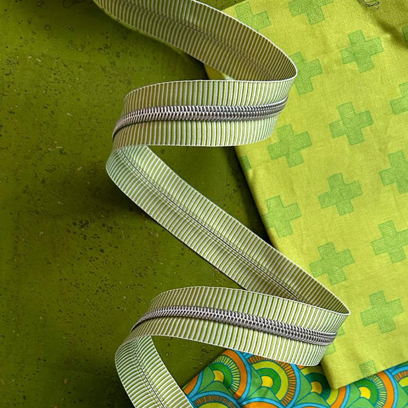 Green and white striped zipper tape with on a green background with green fabric.